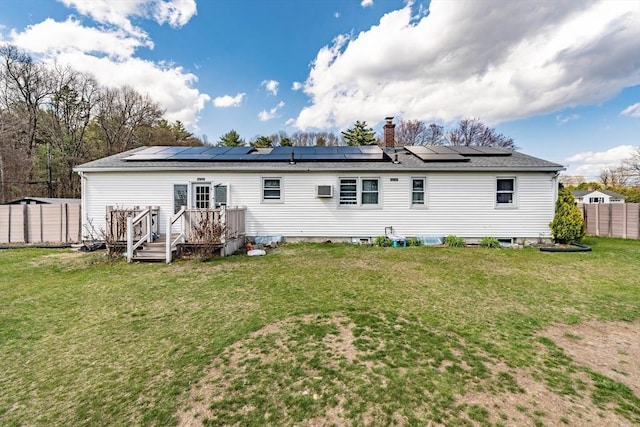 rear view of house featuring a wooden deck, a yard, roof mounted solar panels, and fence