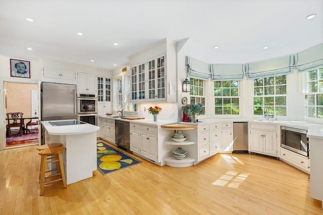 4 Dexter Ln, Manchester, MA 01944 - kitchen featuring stainless steel appliances, light wood-type flooring, open shelves, a kitchen bar, and glass insert cabinets