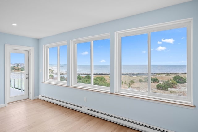 unfurnished room with a water view, light hardwood / wood-style floors, a view of the beach, and a baseboard heating unit