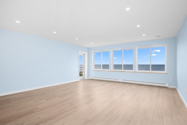 unfurnished room featuring a baseboard radiator, light hardwood / wood-style flooring, a healthy amount of sunlight, and a water view