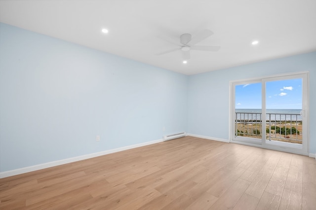 empty room featuring ceiling fan, light hardwood / wood-style flooring, a water view, and a baseboard radiator