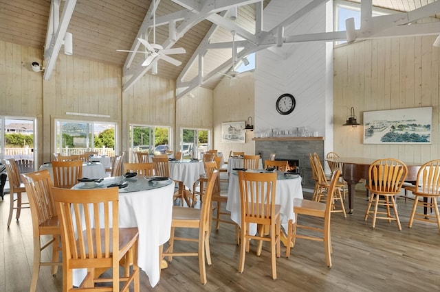 dining area featuring wood walls, high vaulted ceiling, hardwood / wood-style flooring, and ceiling fan