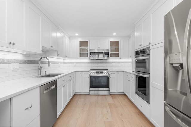 kitchen featuring appliances with stainless steel finishes, light wood-type flooring, light stone counters, sink, and white cabinetry