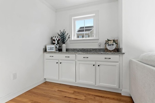 bar with light hardwood / wood-style flooring, white cabinetry, crown molding, and dark stone counters