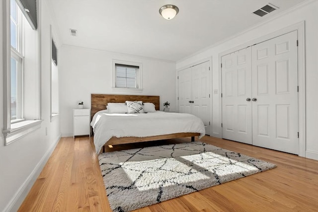 bedroom with multiple windows, multiple closets, light hardwood / wood-style floors, and ornamental molding