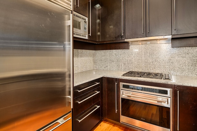 kitchen with light stone countertops, appliances with stainless steel finishes, tasteful backsplash, light hardwood / wood-style floors, and dark brown cabinetry