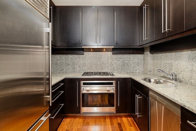 kitchen with light stone countertops, sink, stainless steel appliances, backsplash, and light hardwood / wood-style floors