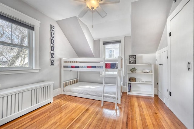 bedroom featuring radiator heating unit, lofted ceiling, hardwood / wood-style floors, baseboards, and ceiling fan