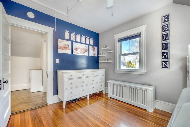 bedroom featuring radiator heating unit, attic access, light wood-style flooring, and baseboards