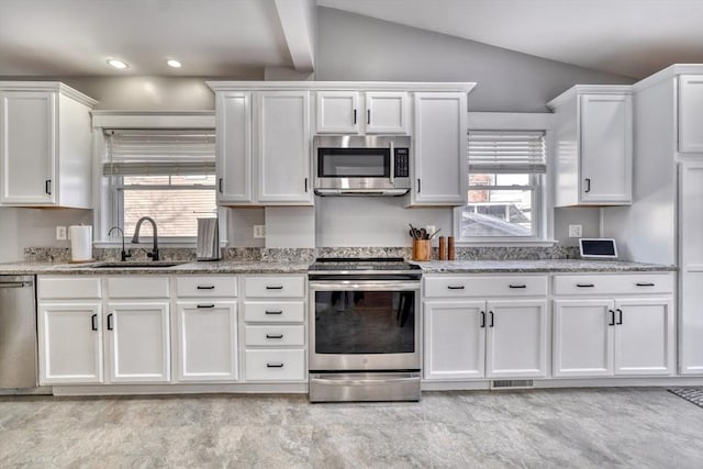 kitchen featuring stainless steel appliances, a sink, lofted ceiling, white cabinetry, and light stone countertops
