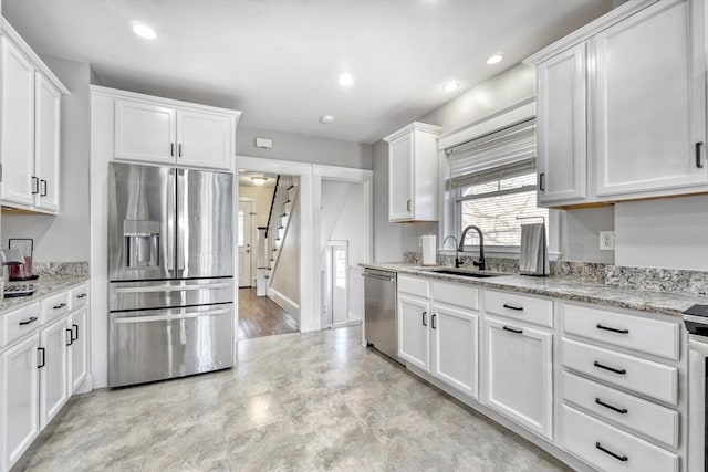 kitchen featuring appliances with stainless steel finishes, a sink, white cabinetry, light stone countertops, and recessed lighting