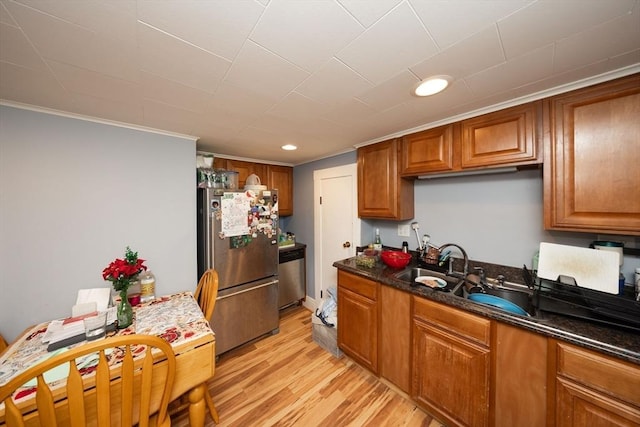 kitchen featuring appliances with stainless steel finishes, crown molding, sink, light hardwood / wood-style flooring, and dark stone countertops