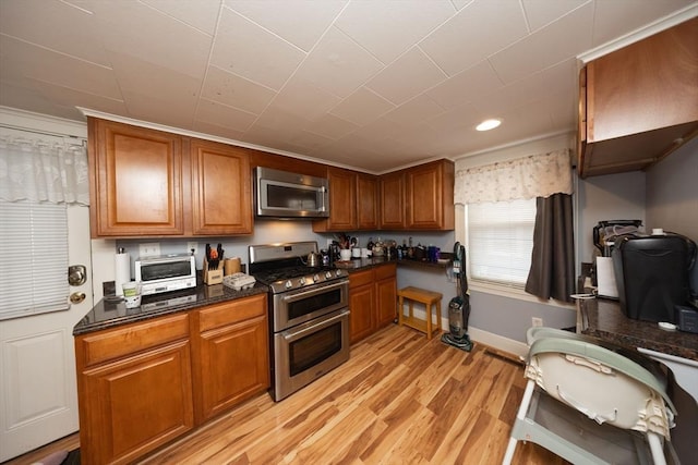 kitchen featuring appliances with stainless steel finishes, light wood-type flooring, and dark stone counters