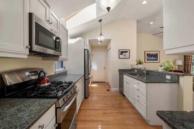 kitchen featuring appliances with stainless steel finishes, light wood-type flooring, vaulted ceiling with skylight, pendant lighting, and white cabinets