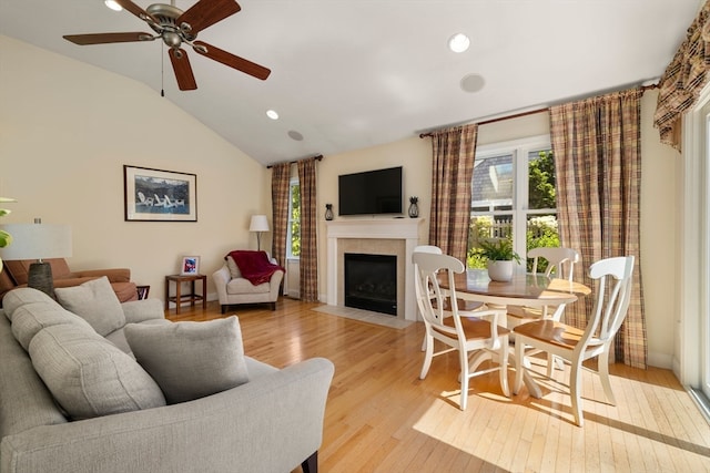 living room featuring ceiling fan, light hardwood / wood-style floors, lofted ceiling, and a tile fireplace