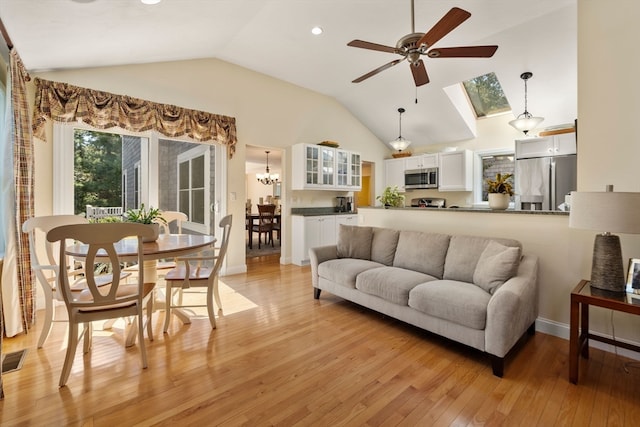 living room with ceiling fan with notable chandelier, light hardwood / wood-style flooring, and lofted ceiling with skylight