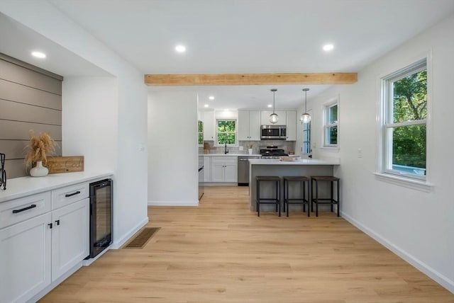 kitchen with appliances with stainless steel finishes, a breakfast bar, white cabinetry, light hardwood / wood-style floors, and wine cooler