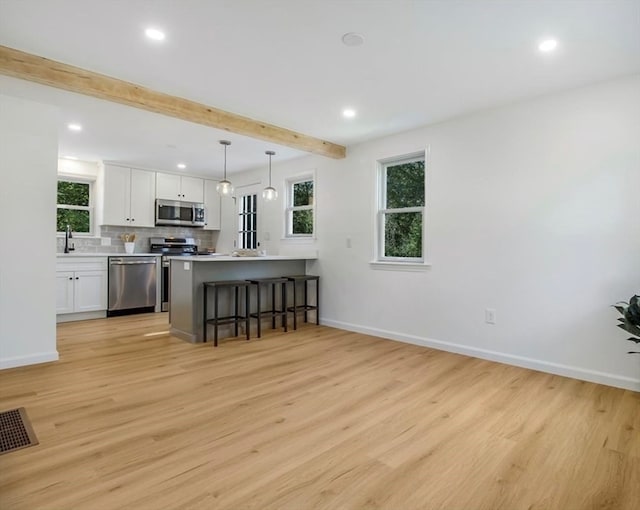 kitchen with white cabinets, beamed ceiling, decorative light fixtures, light hardwood / wood-style floors, and stainless steel appliances