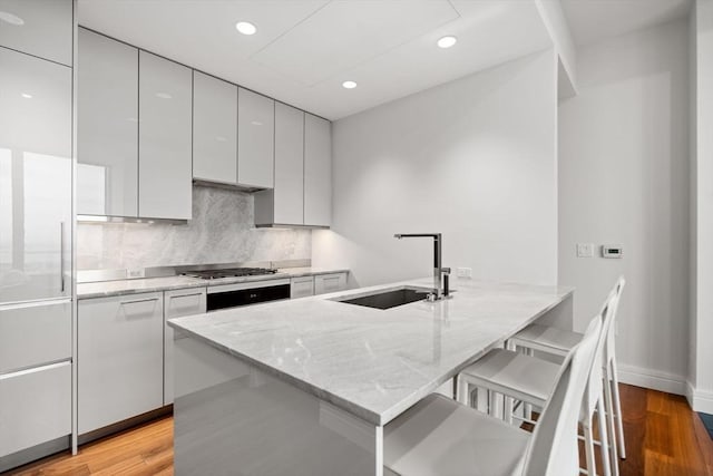 kitchen with sink, light wood-type flooring, a kitchen bar, and light stone counters