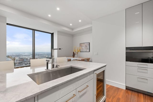 kitchen with white cabinets, beverage cooler, light wood-type flooring, and light stone countertops