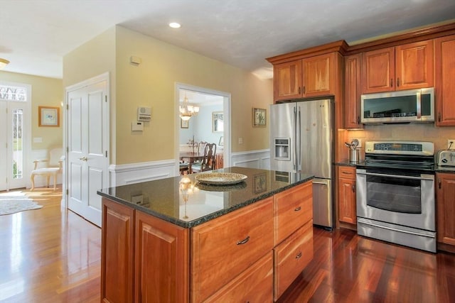 32 Erins Way, Holden, MA 01520 - kitchen featuring appliances with stainless steel finishes, dark wood finished floors, brown cabinetry, wainscoting, and dark stone countertops