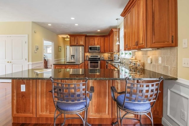 32 Erins Way, Holden, MA 01520 - kitchen with appliances with stainless steel finishes, brown cabinets, a wainscoted wall, a peninsula, and a kitchen island