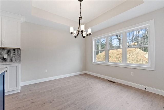 unfurnished dining area featuring a chandelier, visible vents, light wood-style floors, baseboards, and a raised ceiling