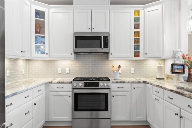 kitchen featuring glass insert cabinets, open shelves, backsplash, white cabinets, and appliances with stainless steel finishes