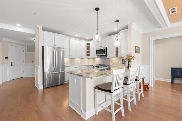 kitchen with glass insert cabinets, visible vents, light stone counters, a peninsula, and appliances with stainless steel finishes