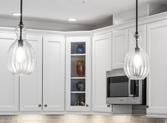 details with stainless steel microwave, white cabinetry, and hanging light fixtures