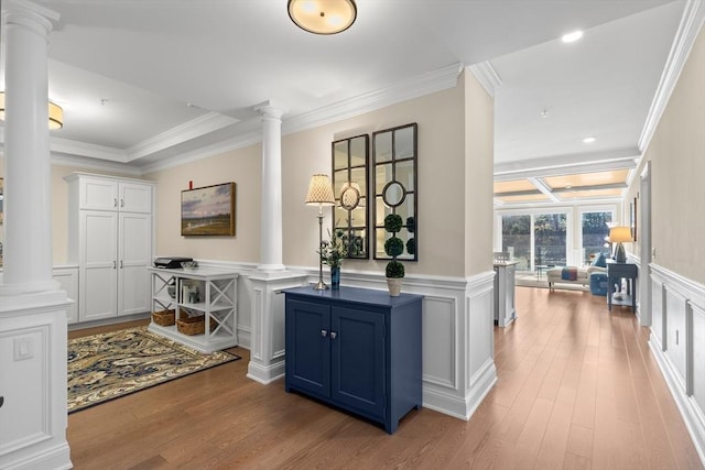 corridor with ornate columns, a decorative wall, wood finished floors, and ornamental molding