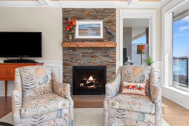 living area with ornamental molding, a stone fireplace, and wood finished floors