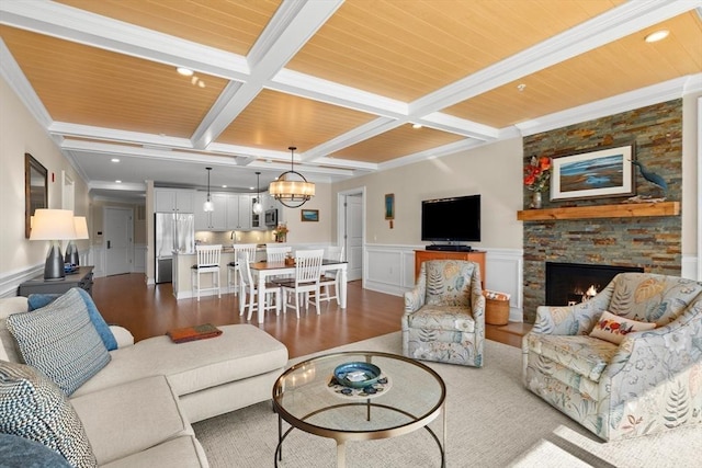 living area with beamed ceiling, a wainscoted wall, coffered ceiling, wood finished floors, and a stone fireplace