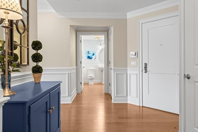interior space with light wood-style flooring, crown molding, and a wainscoted wall