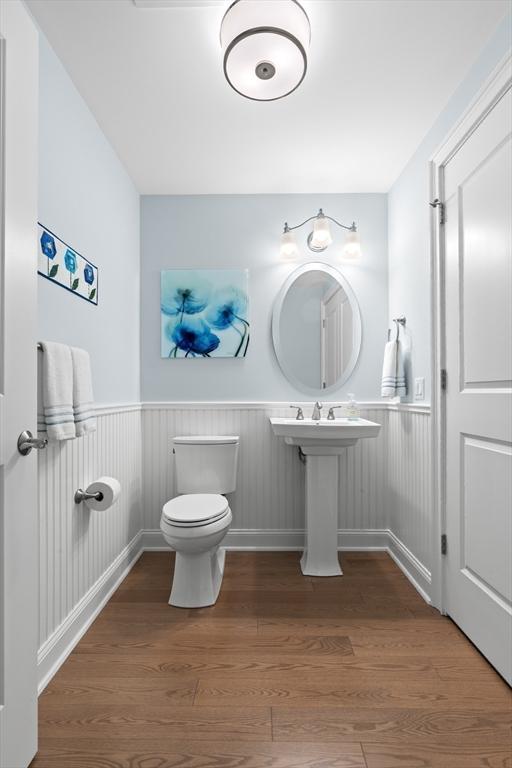 bathroom featuring wood finished floors, toilet, and a wainscoted wall