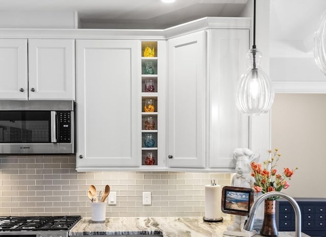 interior space featuring light stone counters, stainless steel microwave, white cabinetry, and backsplash