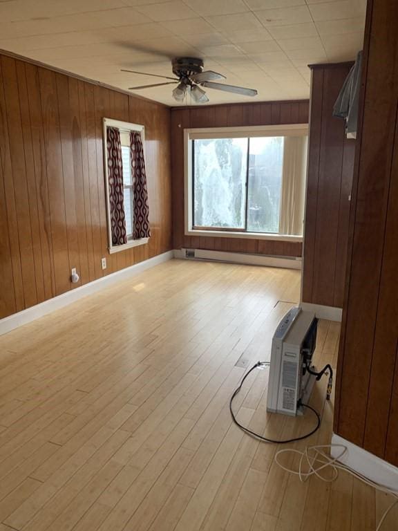 unfurnished living room featuring ceiling fan, wooden walls, a baseboard radiator, and light hardwood / wood-style floors