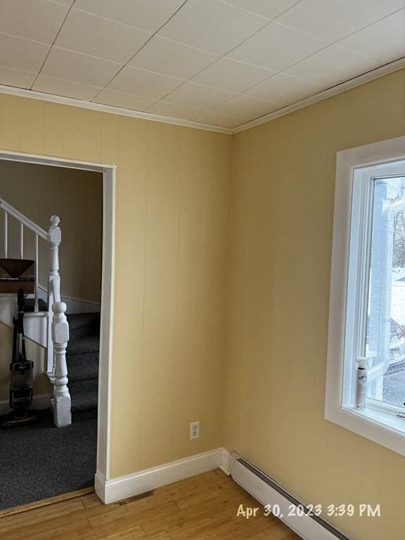 unfurnished room featuring hardwood / wood-style flooring, crown molding, a wealth of natural light, and a baseboard heating unit