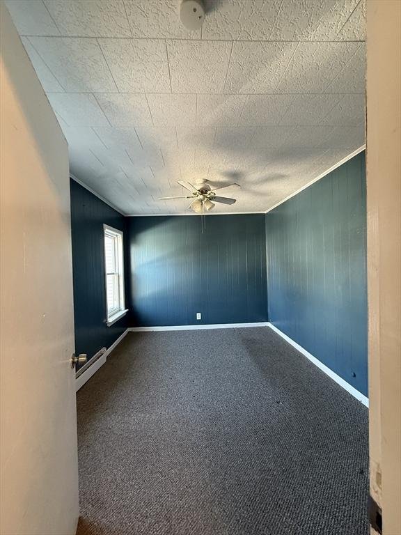 carpeted empty room featuring ceiling fan, wooden walls, and a baseboard heating unit