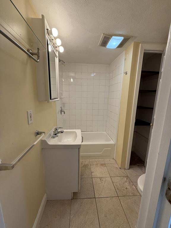 full bathroom with tiled shower / bath, vanity, a textured ceiling, and toilet