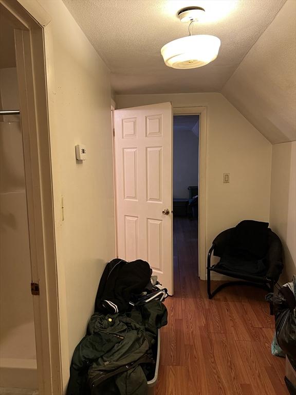 hall with vaulted ceiling, hardwood / wood-style floors, and a textured ceiling