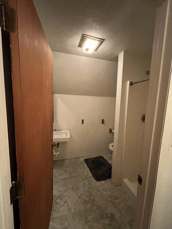 bathroom featuring vaulted ceiling, sink, a textured ceiling, and toilet