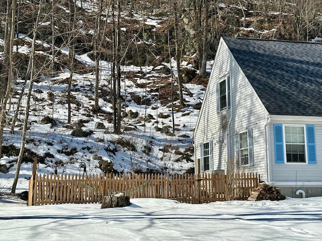 view of snowy exterior featuring a shingled roof and a fenced front yard