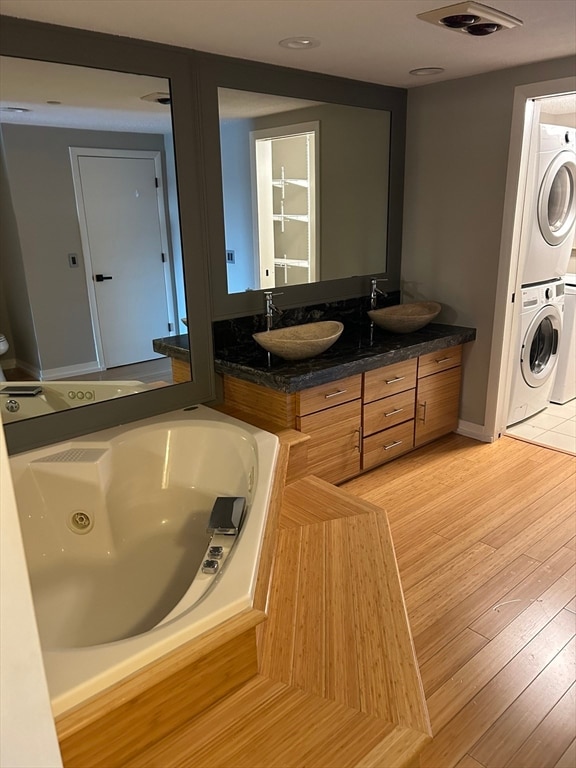 bathroom with hardwood / wood-style floors, stacked washing maching and dryer, a tub to relax in, and vanity