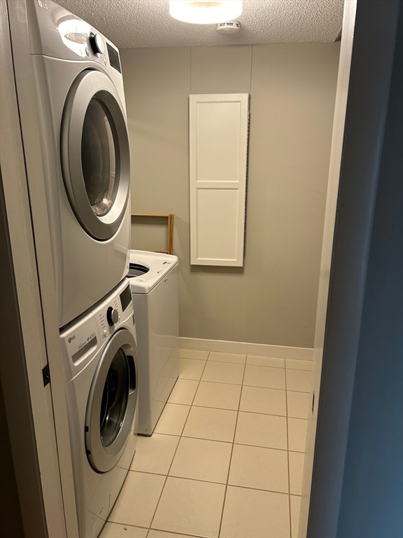 clothes washing area with stacked washer / dryer, a textured ceiling, and light tile patterned floors