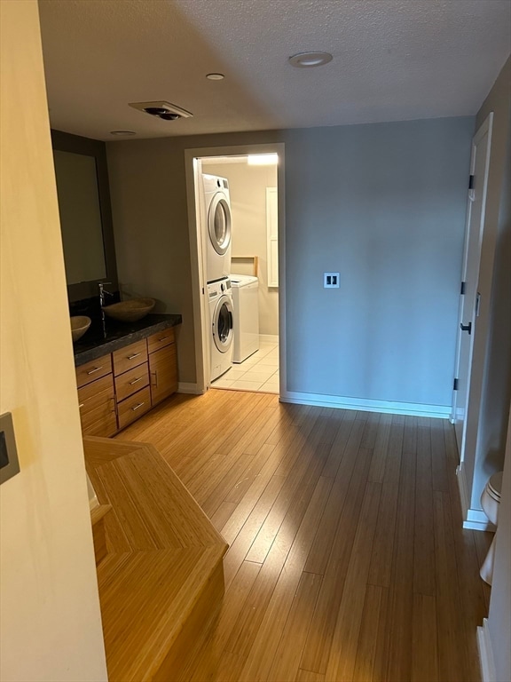 laundry room with a textured ceiling, sink, light hardwood / wood-style flooring, and stacked washer / drying machine