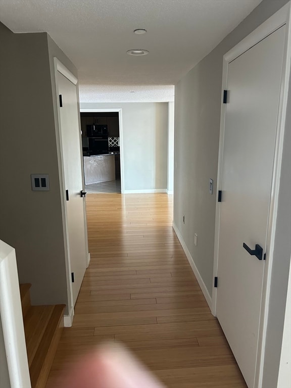 corridor with a textured ceiling and light wood-type flooring