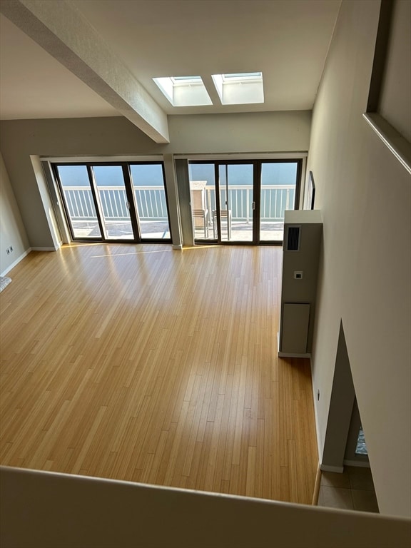 unfurnished living room featuring light wood-type flooring, beamed ceiling, and a skylight