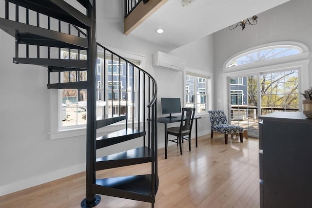stairs with a high ceiling, a wall mounted air conditioner, recessed lighting, baseboards, and wood finished floors