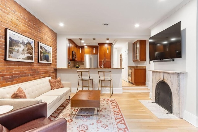 living room with brick wall, a fireplace with flush hearth, baseboards, light wood-style floors, and crown molding